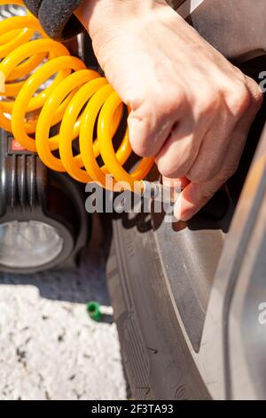 Une femme caucasienne fixe la tubulure en spirale jaune d'un compresseur d'air de voiture 12 v à la valve de tige d'un pneu. Elle vérifie ensuite la pression des pneus et Banque D'Images