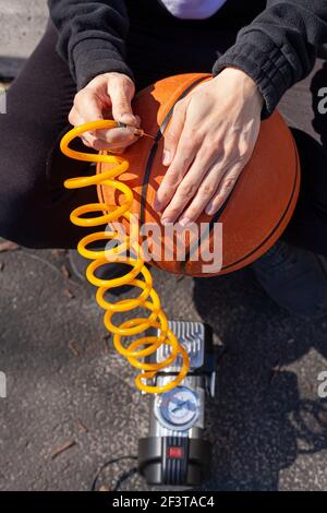 Image en gros plan montrant une femme de race blanche tenant un ballon de basket-ball et en insérant l'embout d'aiguille à l'extrémité de la tubulure fixé au gonfleur de pneu de voiture 12 v sur p Banque D'Images