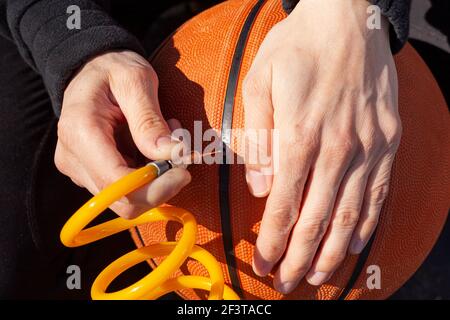 Image en gros plan montrant une femme de race blanche tenant un ballon de basket-ball et en insérant l'embout d'aiguille à l'extrémité de la tubulure fixé au gonfleur de pneu de voiture 12 v sur p Banque D'Images