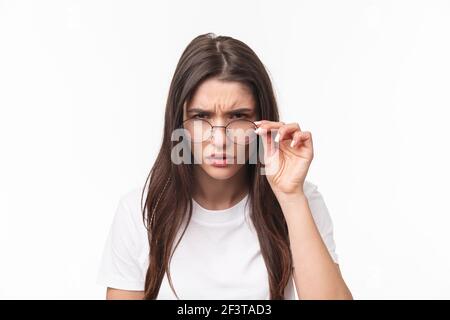 Gros plan portrait d'une jeune femme suspecte et sérieuse, regardez sous les lunettes, en faisant attention à une personne avec une suspicion de méfiance judgmentale, debout Banque D'Images