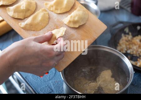 Cuire des boulettes avec des pommes de terre, une femme prend un boulonnage d'une planche en bois et le jette dans une casserole d'eau bouillante, cuisine russe Banque D'Images