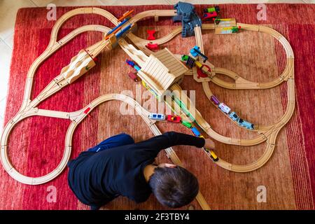 Vue de dessus de l'enfant jouant avec la piste de train en bois moquette à la maison Banque D'Images