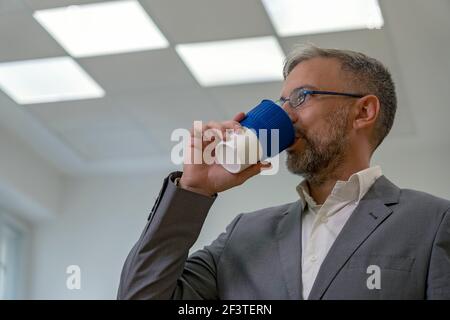 Homme d'affaires ou enseignant debout au bureau pendant l'heure du café. Portrait de l'homme mûr avec une tasse de café. Homme buvant du café. Banque D'Images