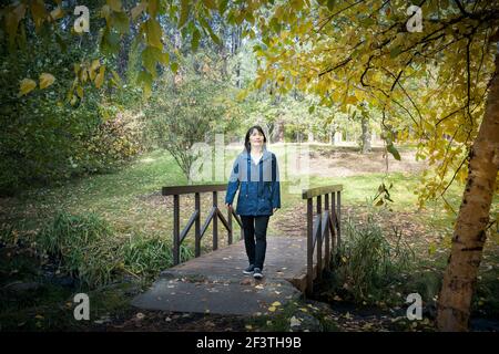 Une femme coréenne traverse une petite passerelle en automne à l'arboretum Finch de Spokane, Washington, États-Unis. Banque D'Images