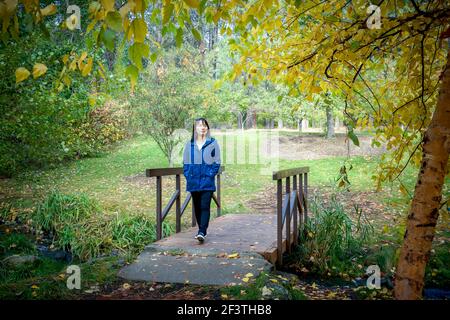 Une femme coréenne traverse une petite passerelle en automne à l'arboretum Finch de Spokane, Washington, États-Unis. Banque D'Images