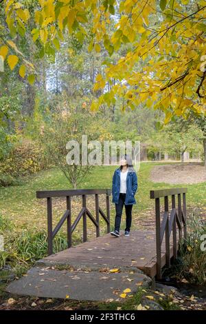 Une femme coréenne traverse une petite passerelle en automne à l'arboretum Finch de Spokane, Washington, États-Unis. Banque D'Images