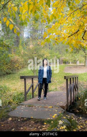 Une femme coréenne traverse une petite passerelle en automne à l'arboretum Finch de Spokane, Washington, États-Unis. Banque D'Images