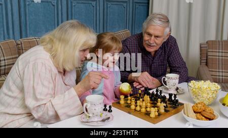 Grand-mère mature grand-père avec enfant fille petit-enfant jouant au jeu d'échecs avec table dans la chambre Banque D'Images