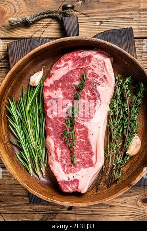 Steak de viande de bœuf frais de New york ou striploin dans une assiette en bois avec des herbes. fond en bois. Vue de dessus Banque D'Images