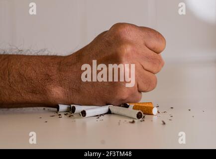 Poing d'un homme frappant une pile de cigarettes cassées sur une table blanche, comme signe de désapprobation et de rejet du tabac. 31 mai, journée internationale sans Banque D'Images