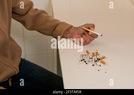 Main d'un homme tenant une cigarette en plastique pour arrêter de fumer, à côté d'une pile de cigarettes cassées comme signe de rejet du tabac sur une table blanche. Banque D'Images