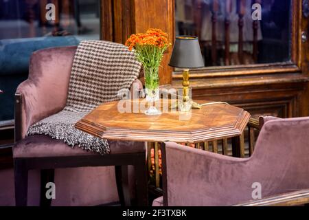 une table en bois avec un vase en verre et des fleurs et une lampe sur la terrasse du café avec des chaises confortables et une couverture près de la fenêtre avec un cla en bois Banque D'Images