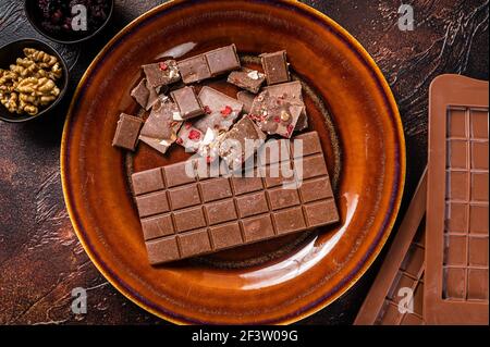Chocolat au lait maison aux noisettes, cacahuètes, canneberges et framboises séchées sur une assiette rustique. Arrière-plan sombre. Vue de dessus Banque D'Images