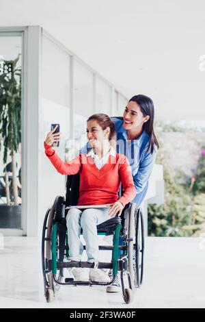 Jeune femme latine en fauteuil roulant prenant une photo de selfie à Lieu de travail avec une autre femme au Mexique Banque D'Images