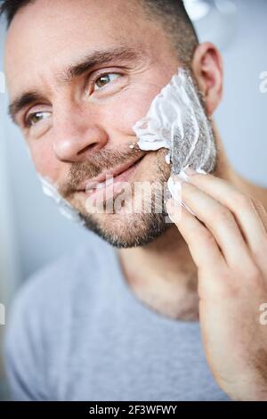 Jeune homme souriant appliquant de la crème à raser sur le visage Banque D'Images