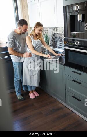 Couple heureux utilisant un ordinateur portable moderne dans la cuisine Banque D'Images