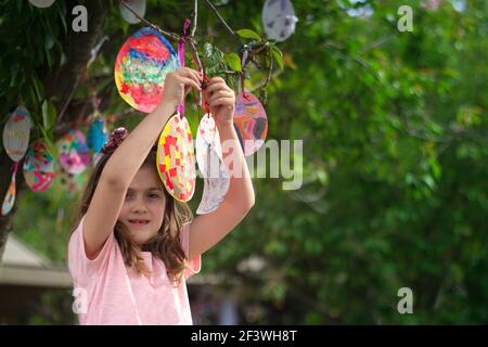 Jolie petite fille accrochée sur l'arbre ses cartes de Pâques en forme d'oeuf, pour la bonne chance et avec de bons voeux Banque D'Images