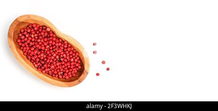 Grains de poivre rouge ou rose dans un petit bol en bois, certains éparpillés à bord près, photo de gros plan du dessus isolée avec fond blanc Banque D'Images