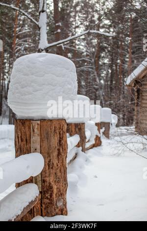 Large snow caps on the stumps of the fence in winter. A wooden fence protects the territory of the house. Banque D'Images