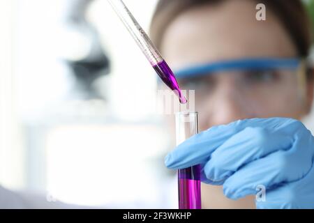 Le chercheur goutte le liquide violet de la pipette dans le tube à essai Banque D'Images