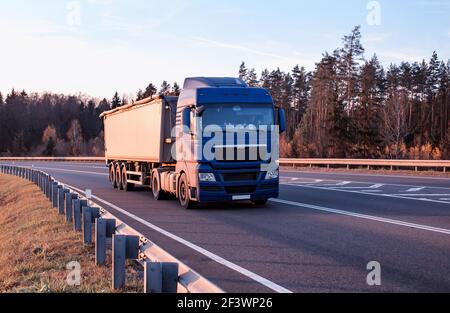 Un camion moderne transporte des cargaisons en vrac le long d'une route asphaltée sur fond de forêt et de ciel. Concept pour le transport de la carg en vrac solide Banque D'Images