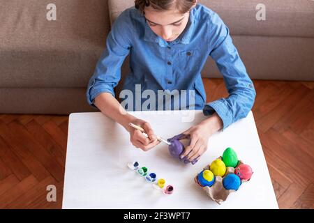 Une jeune fille de neuf ans en chemise bleue peint des œufs à une table blanche. Concept de Pâques. Mise au point sélective. Banque D'Images