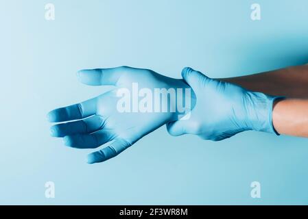 Le médecin porte des gants chirurgicaux stérilisés bleus sur fond bleu. Copier l'espace. Journée nationale des médecins. Journée internationale des infirmières. Protection de la santé Banque D'Images