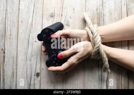 Les mains d'une jeune femme aux ongles rouges sont attachées et reposent sur un fond en bois clair, elle tient une manette de jeu dans ses mains, concept sur addic Banque D'Images