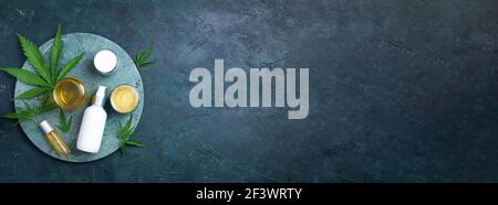 Composition de la couche plate avec feuilles de chanvre, huile, produits cosmétiques, crème pour le visage, beurre de corps sur le marbre sur fond sombre. Vue de dessus, espace de copie Banque D'Images