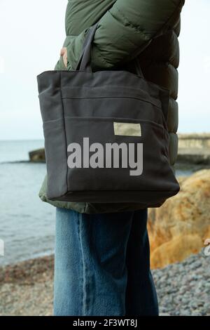 Femme en vêtements d'hiver avec un sac éco élégant sur le bord de la mer, concept de mode de vie durable Banque D'Images