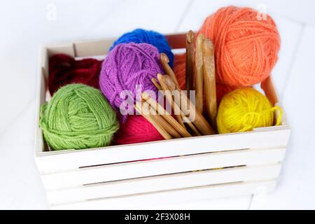Vue de dessus d'une boîte en bois avec des crochets en bambou naturel et des boules de laine de différentes couleurs. Banque D'Images