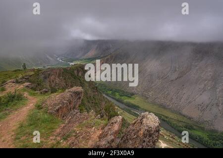 Vue panoramique sur les montagnes, la vallée entre les montagnes, la forêt, la rivière sinueuse et le brouillard sur fond de ciel couvert et de nuages en été. Banque D'Images