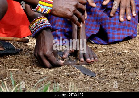 Gros plan de Massai tribesmen faire feu à l'aide d'une perceuse à main et des bâtons de bois. Masai Mara, Kenya, Afrique Banque D'Images