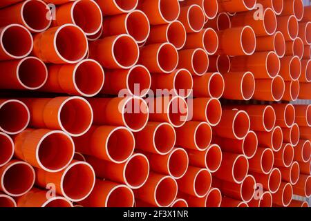 Une pile de tuyaux de conduit en PVC électrique orange dans les lignes d'une extrémité d'entrepôt sur donnant des répétitions de cercles. Banque D'Images