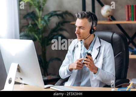 Consultation médicale en ligne. Un médecin généraliste masculin en uniforme médical et un casque, consulte un patient à distance, prescrit un médicament, mène une consultation par ordinateur Banque D'Images