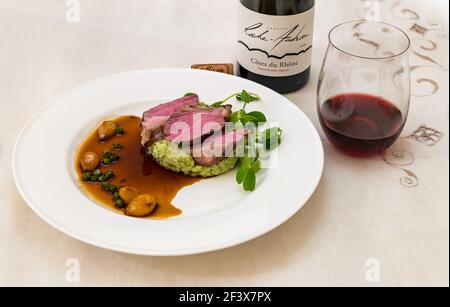 Agneau au risotto, petits pois et oignons caramélisés, verre de vin et bouteille de vin rouge Côte du Rhône Roche Audran Banque D'Images