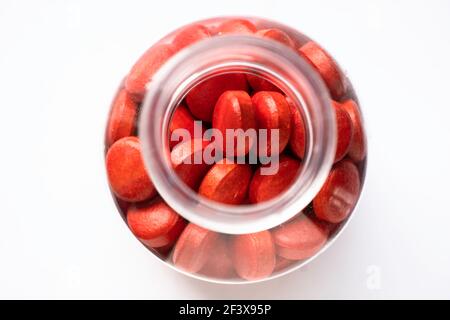 Flacon en verre ou en plastique à col étroit, rempli de pilules rouges et de comprimés isolés sur fond blanc. Vue rapprochée du dessus, mise au point sur le dessus Banque D'Images