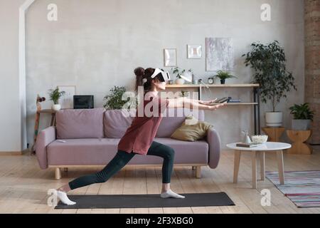 Jeune femme en VR lunettes s'exerçant dans la chambre à regarder entraînement sportif de réalité virtuelle Banque D'Images