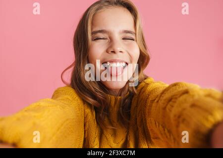 Amuse belle fille montrant sa langue tout en prenant la photo de selfie isolé sur fond rose Banque D'Images