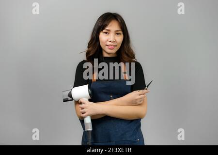 Portrait d'asiatique magnifique gai jeune femme professionnelle coiffeur tenant sèche-cheveux souriant à la caméra posant à son studio de beauté. Banque D'Images