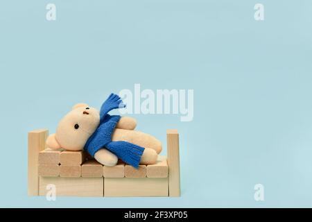 Un ours en peluche allongé dans un berceau en cubes de bois. Sur fond bleu clair. Banque D'Images