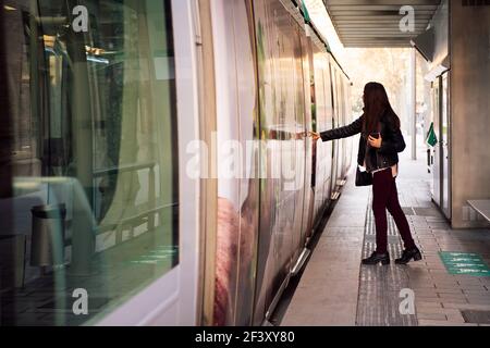 jeune femme appuyant sur le bouton de la porte pour ouvrir la porte et monter à bord du tramway, concept de transport en commun et de style de vie urbain Banque D'Images