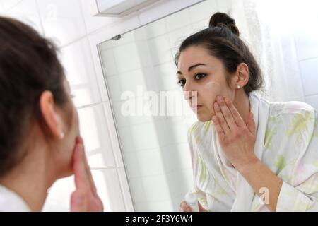 Munich, Allemagne. 18 mars 2021. Une jeune femme se tient devant le miroir et élimine le maquillage, élimine le maquillage, crème, applique la lotion, le maquillage, soins du visage, soins du corps, maquillage, maquillage. Modèle visage, Beauté, Beauté publié | utilisation dans le monde crédit : dpa/Alamy Live News Banque D'Images