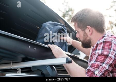 L'homme met des choses dans le porte-bagages de toit d'une voiture ou dans une caisse, lors d'une soirée d'été. Voyage en famille. Banque D'Images