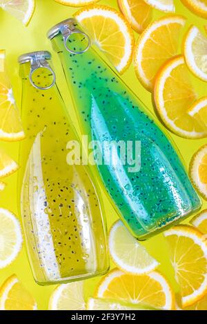 Boissons bleues et jaunes aux graines dans des bouteilles de verre sur fond tropical, faites à partir d'une tranche de smoothie à l'orange et au citron. Boisson froide dans l'eau. Été le Banque D'Images