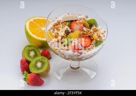 Yaourt avec granola et fruits comme fraise, raisin, banane, papaye, orange, kiwi dans un bol en verre sur fond blanc. Une alimentation saine. Banque D'Images