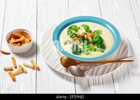 soupe à la crème avec brocoli et croûtons dans un bol bleu sur une table blanche en bois avec des cuillères, vue horizontale d'en haut Banque D'Images