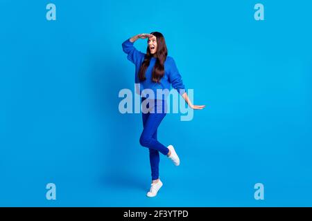 Photo pleine grandeur de brunette optimiste femme mignonne regard loin portez un pantalon chandail bleu avec des sneakers isolées sur fond lumineux Banque D'Images