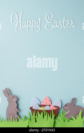 Happy Easter carte de vœux faite à la main avec des lapins en papier, des œufs décorés et de l'herbe verte. Espace pour le texte. Vue de dessus avec espace de copie. Orientation verticale Banque D'Images