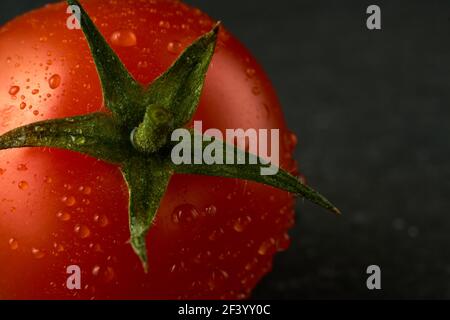 Une seule tomate rouge cerise sur un panneau en pierre noire avec un fond en bois. Peut également servir d'arrière-plan ou de texture. Banque D'Images